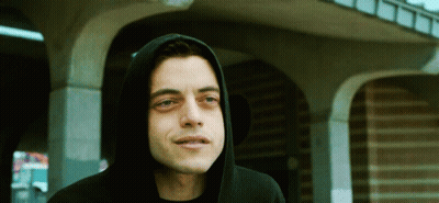 A Man Wearing A Black Hoodie Stands In Front Of A Brick Building GIF
