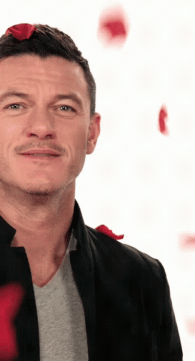 A Man Wearing A Black Jacket And A Grey Shirt With Red Roses On His Head GIF