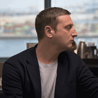A Man Wearing A Black Jacket And A Grey Sweater Looks Out A Window GIF