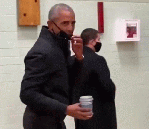 A Man Wearing A Black Jacket And A Mask Is Holding A Cup Of Coffee . GIF