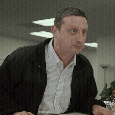 A Man Wearing A Black Jacket And A Plaid Shirt Looks At Something GIF
