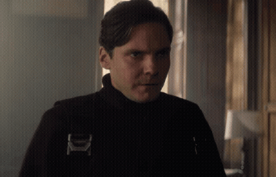 A Man Wearing A Black Jacket With The Letter K On It Looks At The Camera GIF