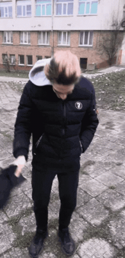 A Man Wearing A Black Jacket With The Number 1 On It Is Standing In Front Of A Building GIF