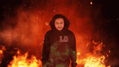 A Man Wearing A Black La Hoodie Stands In Front Of Flames GIF
