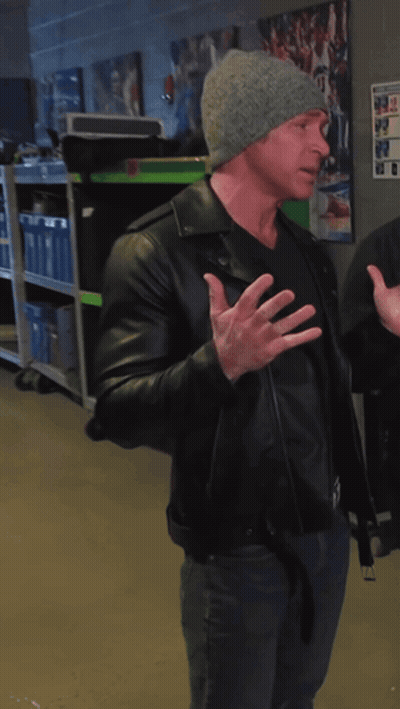 A Man Wearing A Black Leather Jacket And A Gray Hat Stands In A Room GIF