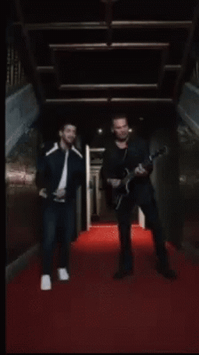 A Man Wearing A Black Leather Jacket And A White T-Shirt Is Standing With His Arms Outstretched . GIF