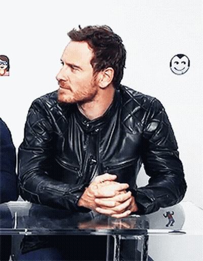 A Man Wearing A Black Leather Jacket Is Sitting At A Table With His Hands Folded GIF