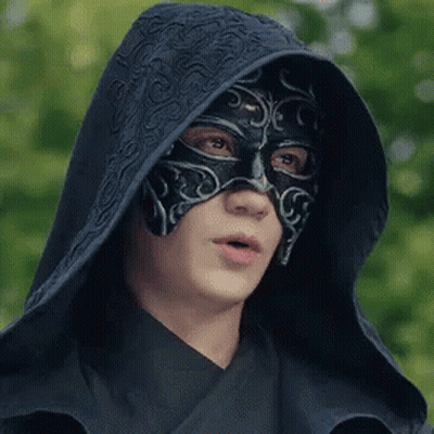 A Man Wearing A Black Mask And A Hood Is Looking At The Camera . GIF