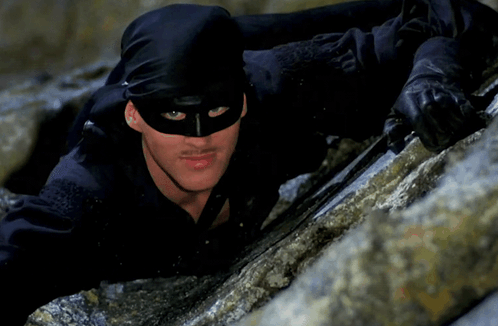 A Man Wearing A Black Mask And Gloves Is Climbing Up A Rock GIF