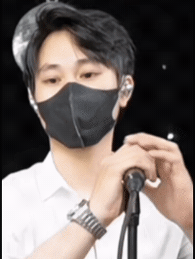 A Man Wearing A Black Mask Is Holding A Microphone In Front Of Him . GIF