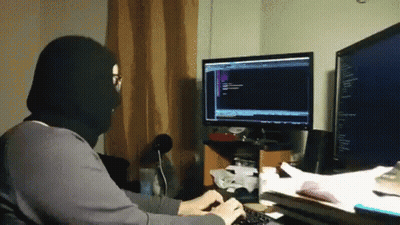 A Man Wearing A Black Mask Is Typing On A Keyboard In Front Of A Computer Monitor . GIF