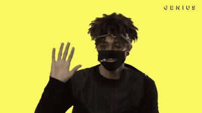 A Man Wearing A Black Mask Is Waving His Hand In Front Of A Yellow Background With The Word Genius On It GIF