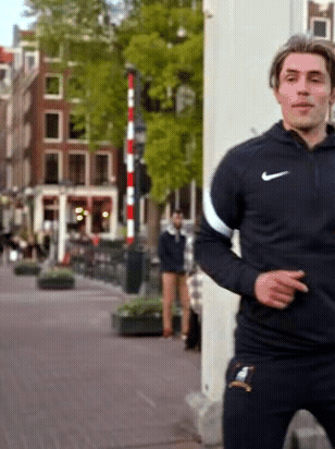 A Man Wearing A Black Nike Jacket Is Standing On A Street GIF