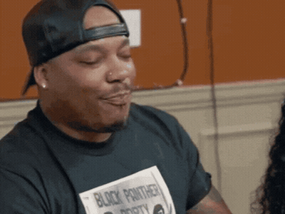 A Man Wearing A Black Panther Shirt Is Making A Face GIF