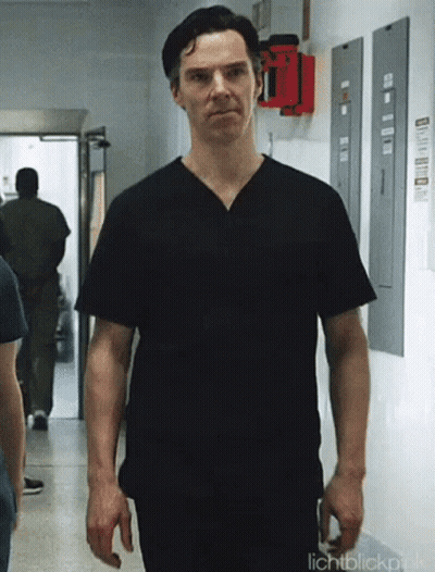 A Man Wearing A Black Scrub Top Is Walking Down A Hallway . GIF