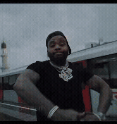 A Man Wearing A Black Shirt And A Hat Is Standing In Front Of A Car . GIF