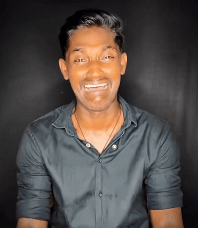 a man wearing a black shirt and a necklace smiles for the camera
