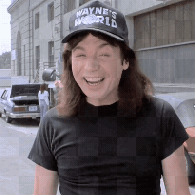 A Man Wearing A Black Shirt And A Wayne 'S World Hat Smiles GIF