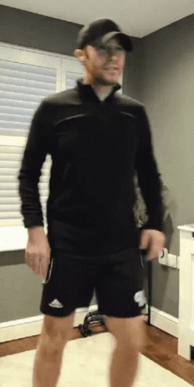 A Man Wearing A Black Shirt And Black Shorts Is Standing In A Room GIF