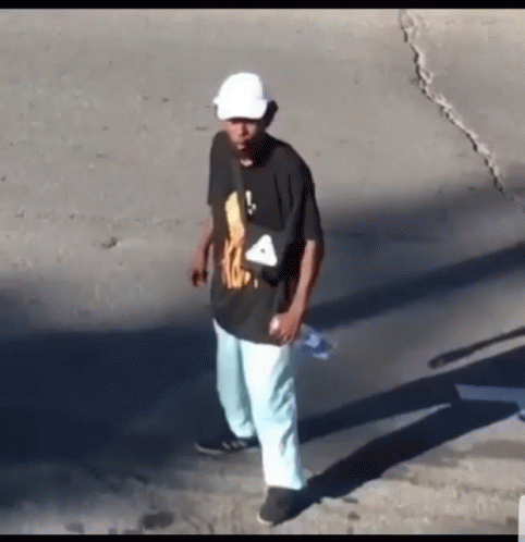 A Man Wearing A Black Shirt And Blue Pants Is Walking Down The Street . GIF