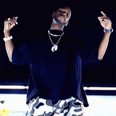 A Man Wearing A Black Shirt And White Camo Shorts Is Making A Peace Sign GIF