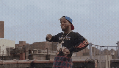 A Man Wearing A Black Shirt That Says " Die " Is Standing On A Rooftop . GIF