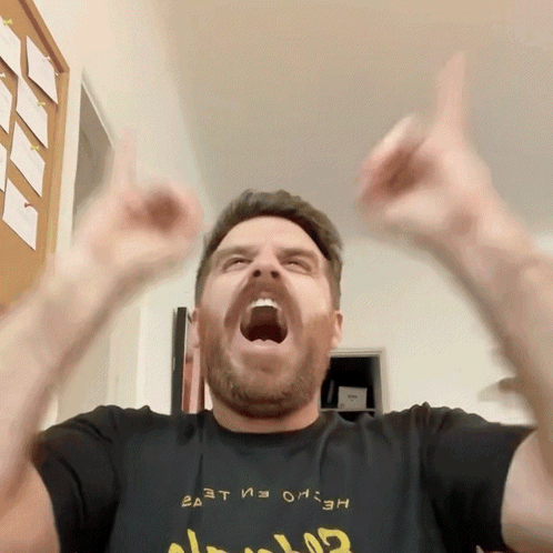 A Man Wearing A Black Shirt That Says ' Ea At ' On It Is Raising His Arms In The Air GIF