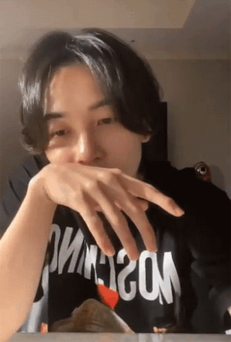 A Man Wearing A Black Shirt That Says Moschino Covering His Mouth With His Hand GIF