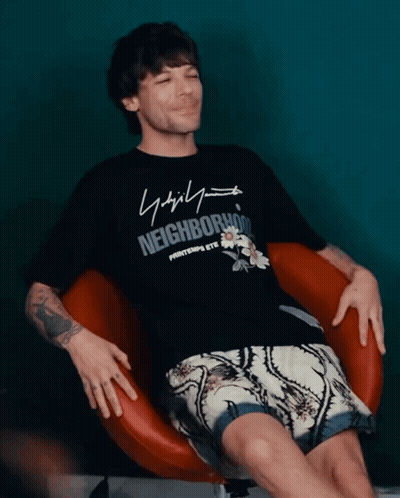 A Man Wearing A Black Shirt That Says Neighborhood Sits In A Chair GIF