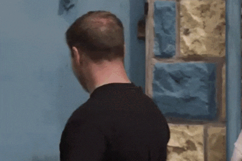 A Man Wearing A Black Shirt That Says Reclaimed Stands In Front Of A Blue Door GIF