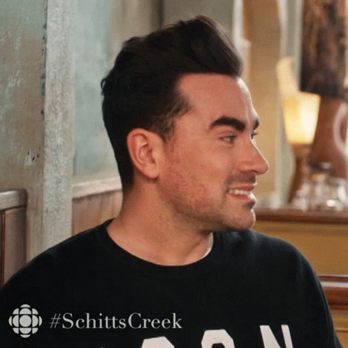 A Man Wearing A Black Shirt That Says Schitts Creek On It GIF