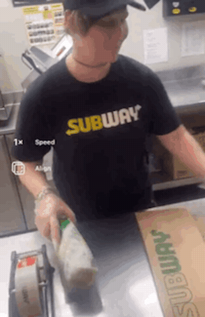 A Man Wearing A Black Shirt That Says Subway Is Standing At A Counter GIF