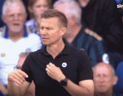 A Man Wearing A Black Shirt With A Blue Circle On It Stands In Front Of A Crowd GIF
