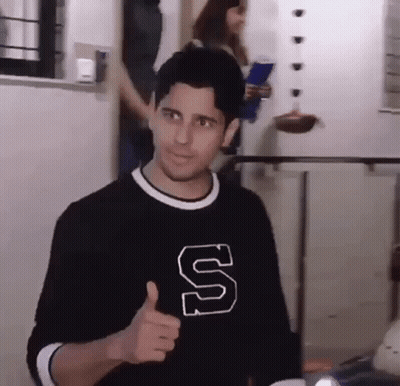 A Man Wearing A Black Shirt With A Letter S On It Is Giving A Thumbs Up . GIF
