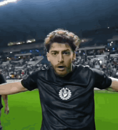 A Man Wearing A Black Shirt With A Shield On It GIF