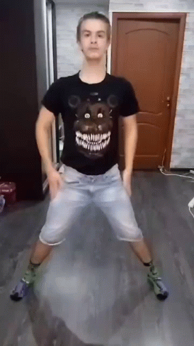 A Man Wearing A Black Shirt With A Teddy Bear On It Is Dancing In A Living Room . GIF
