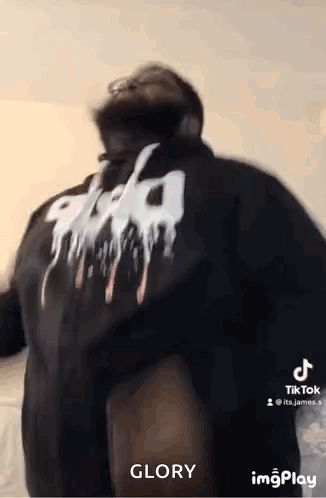 A Man Wearing A Black Shirt With A White Logo On The Back Is Dancing . GIF