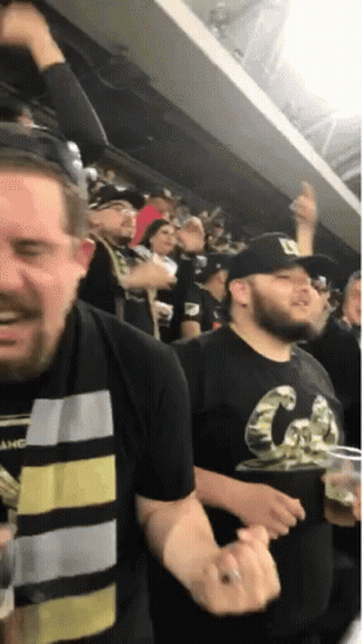 A Man Wearing A Black Shirt With The Letter D On It Stands In A Crowd GIF