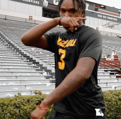 A Man Wearing A Black Shirt With The Number 3 On It Stands In Front Of A Stadium GIF