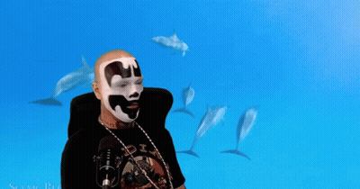 A Man Wearing A Black Shirt With The Word Six On It Stands In Front Of Dolphins GIF