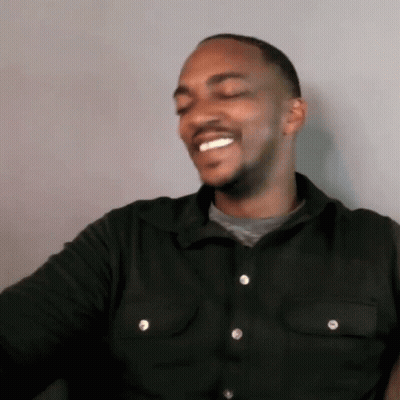 A Man Wearing A Black Shirt With White Buttons Is Smiling GIF