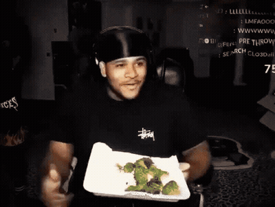 A Man Wearing A Black Stussy Shirt Is Holding A Plate Of Broccoli In His Hands GIF