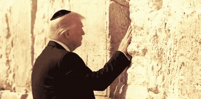 A Man Wearing A Black Suit And A Yarmulke Stands In Front Of A Stone Wall GIF