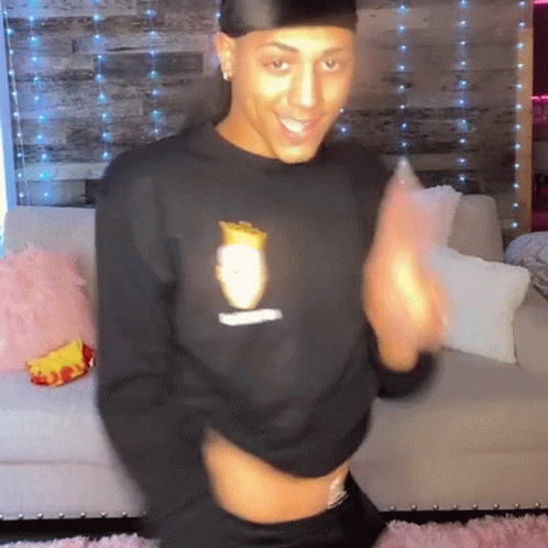 A Man Wearing A Black Sweatshirt With A Picture Of A Man On It Is Dancing On A Couch . GIF
