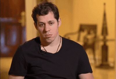 A Man Wearing A Black T-Shirt Is Sitting In Front Of A Chair GIF