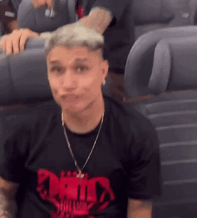 A Man Wearing A Black T-Shirt With A Red Skull On It Is Sitting On A Plane Making A Face . GIF