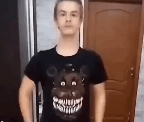 A Man Wearing A Black T-Shirt With A Teddy Bear On It Is Standing In Front Of A Door . GIF