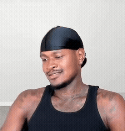 A Man Wearing A Black Tank Top And A Black Headband Is Sitting On A Couch . GIF