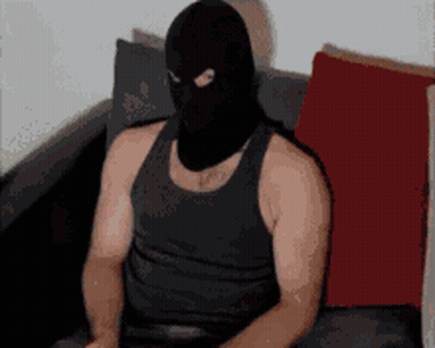 A Man Wearing A Black Tank Top And A Black Mask Is Sitting On A Couch GIF