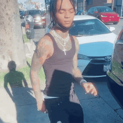 A Man Wearing A Black Tank Top Is Standing In Front Of A White Toyota GIF